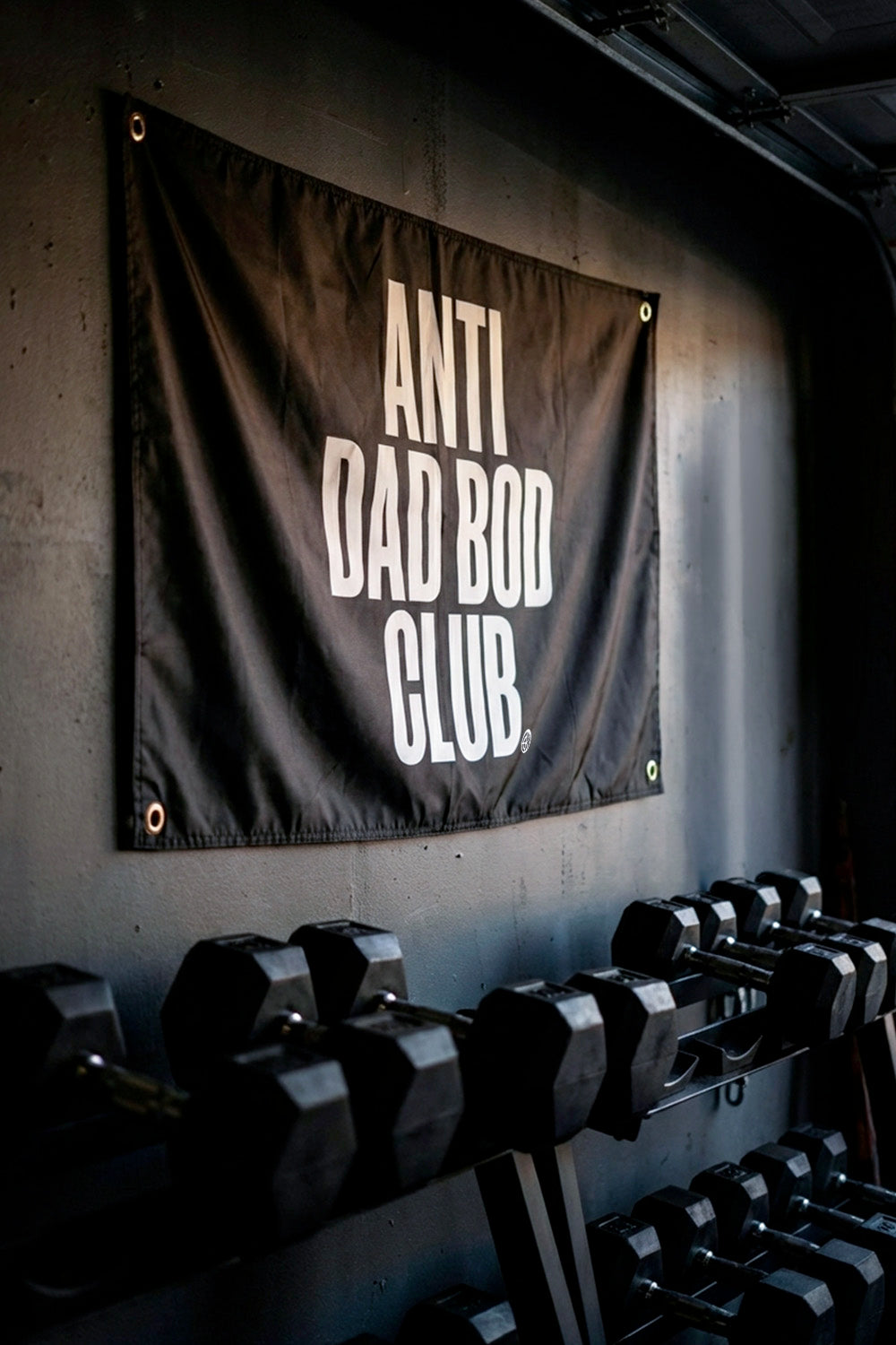 Dumbbells with an 'Anti Dad Bod Club' banner on a wall