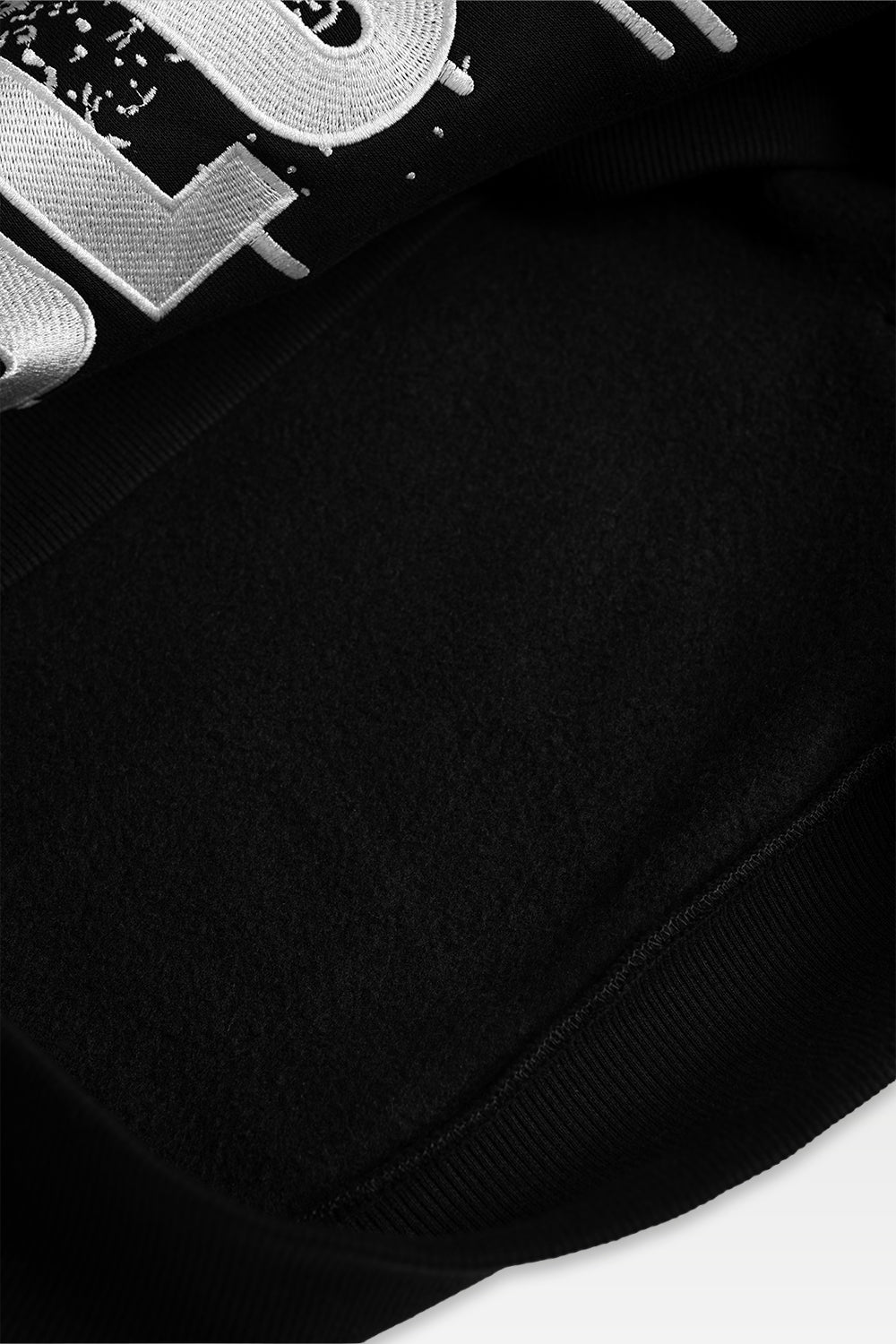 Close-up detail of a black sweatshirt featuring a large white embroidered graphic lettering.
