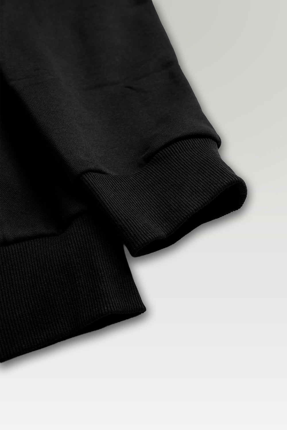 Close-up detail of a black ribbed knit garment, showing the cuff and sleeve construction on a light gray background.
