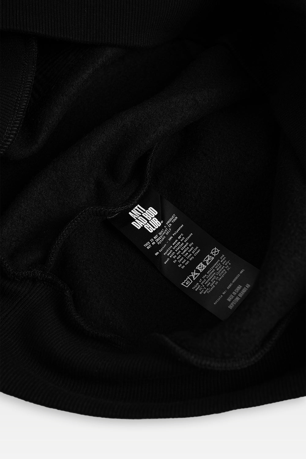 Close-up of a black garment interior showing a sewn-in care label with white text and logo on black fabric.