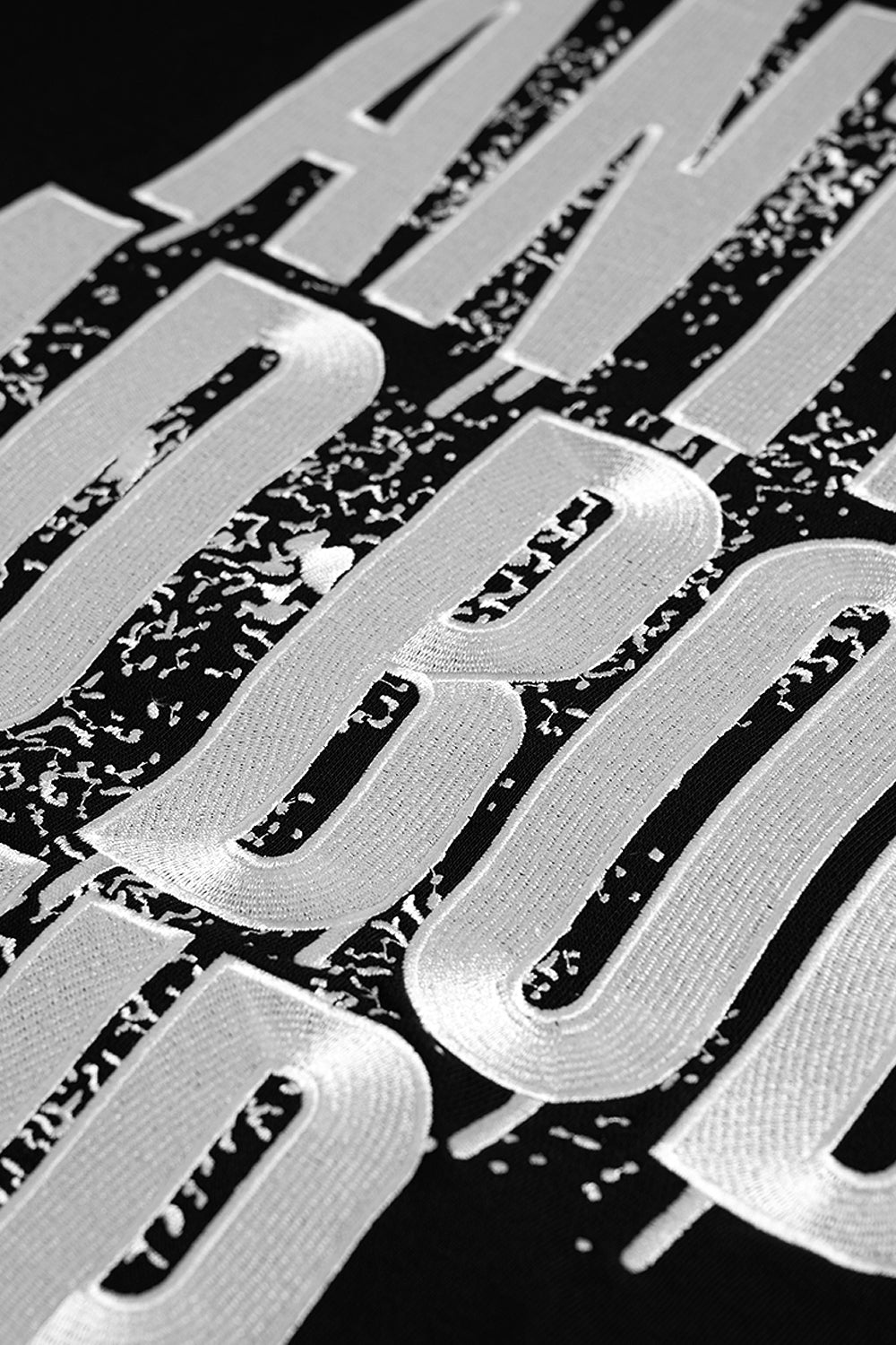 A close-up of a black garment featuring large, white embroidered letters with a distressed, textured pattern.