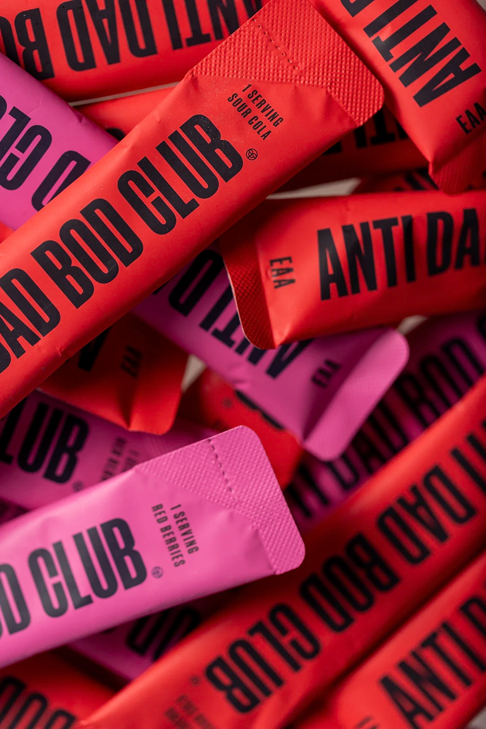 Close-up of 'Anti Bad Bod Club' Amino Acid sachets in pink and red packaging.