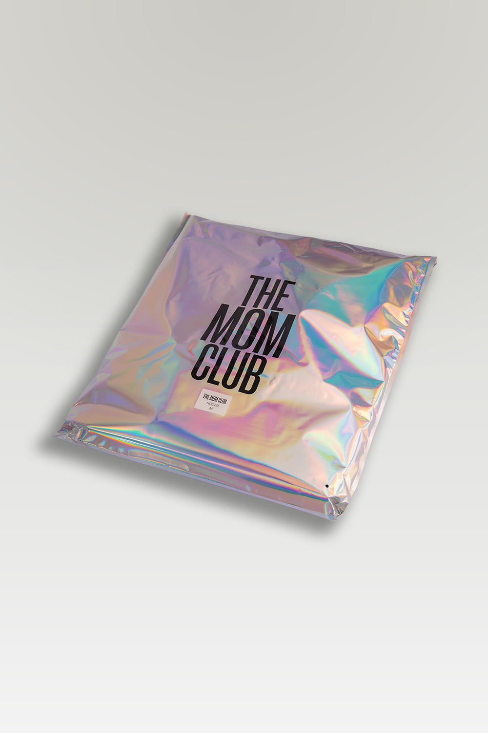 An iridescent holographic zippered pouch with black text reading 'THE MOM CLUB' shown on a light gray background.