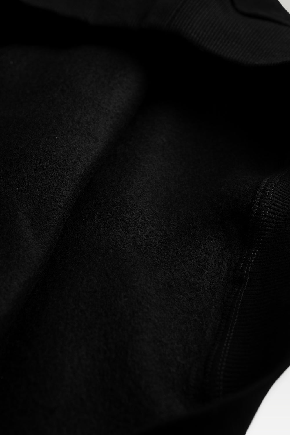 Close-up detail shot of a black textured fabric garment, showing a ribbed knit collar and a cuff seam.