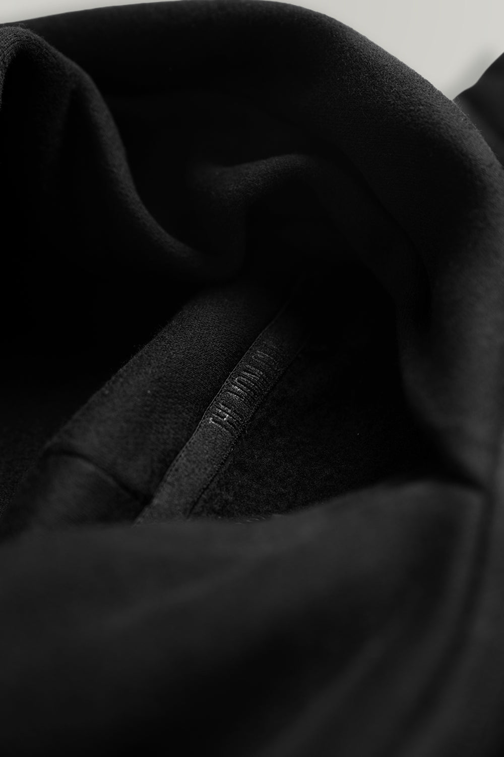 Close-up detail of a black hooded sweatshirt showing the interior lining and a small tonal printed logo on the inner cuff.