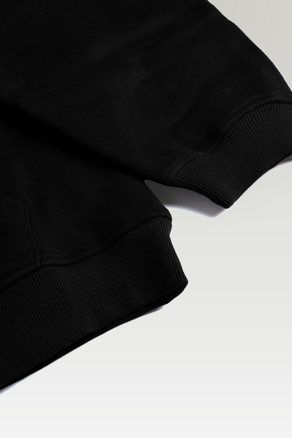 Close-up detail of a black ribbed knit garment, showing the texture and construction of the cuff on a light gray background.